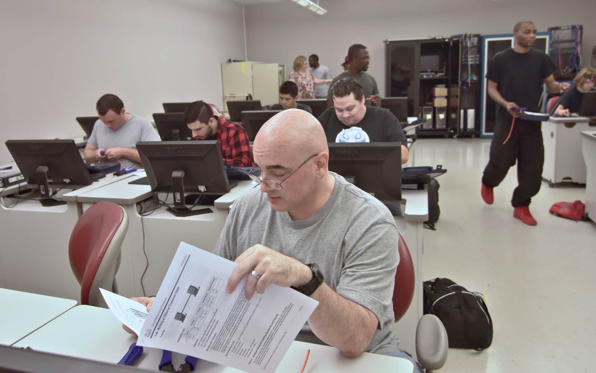 A cybersecurity training class: people at workstations, one reading through a printed exercise.