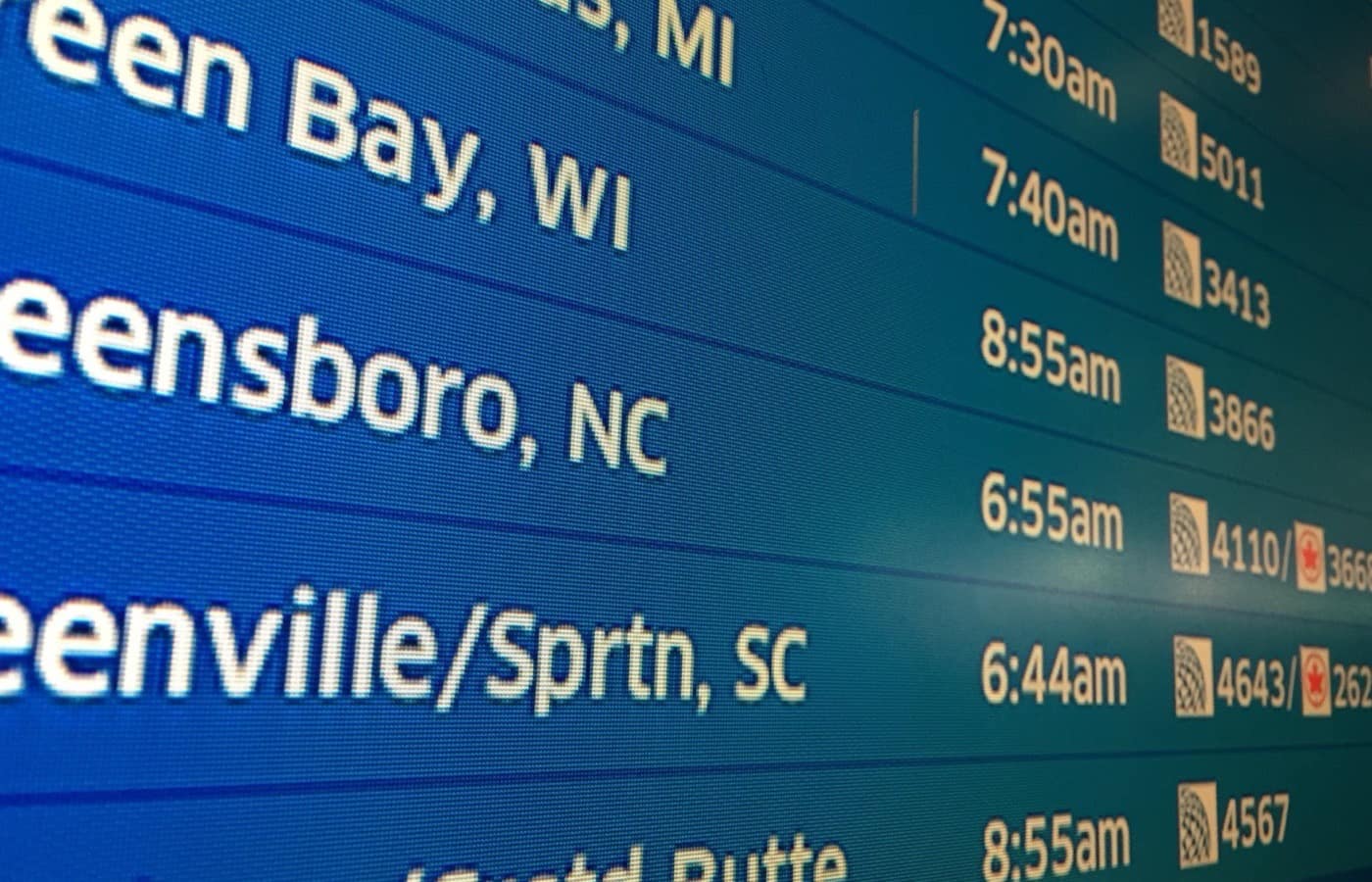 An airport departure board, destinations and times running down the screen.