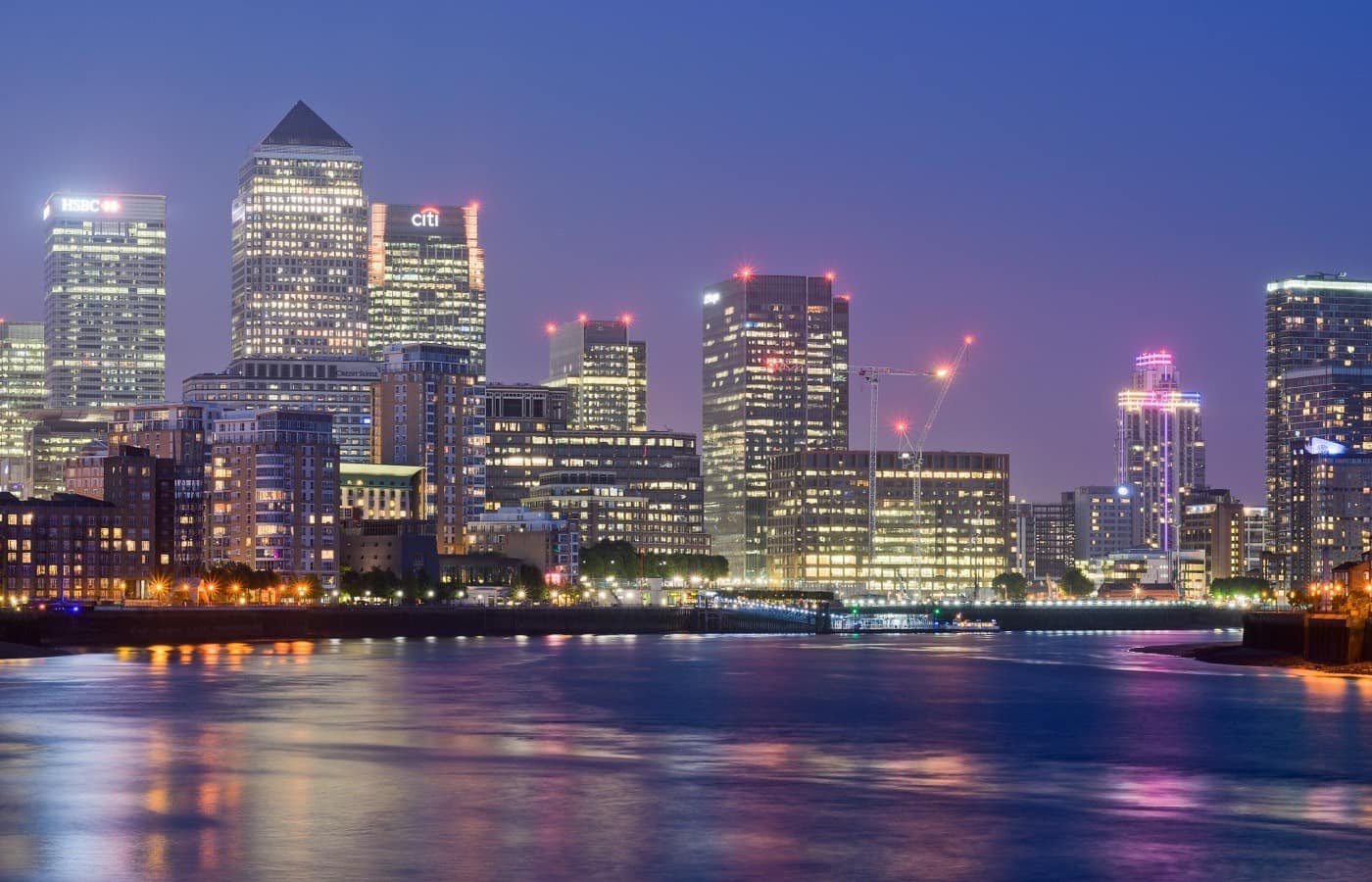 Bank towers lit at night above a river, their reflections broken on the water.