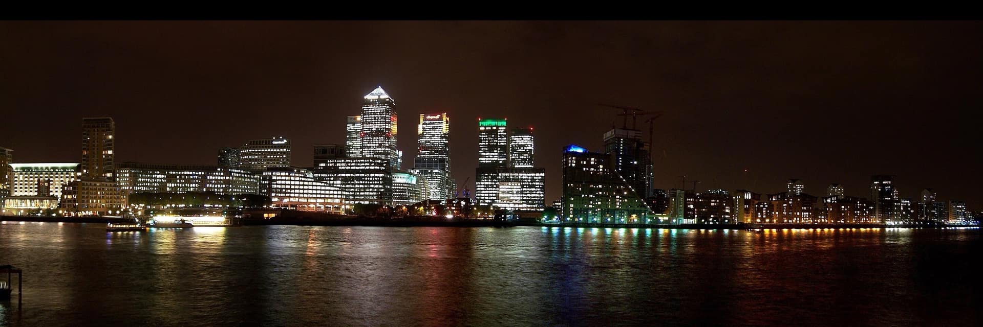 A financial district at night across the water, every floor of every tower still lit.