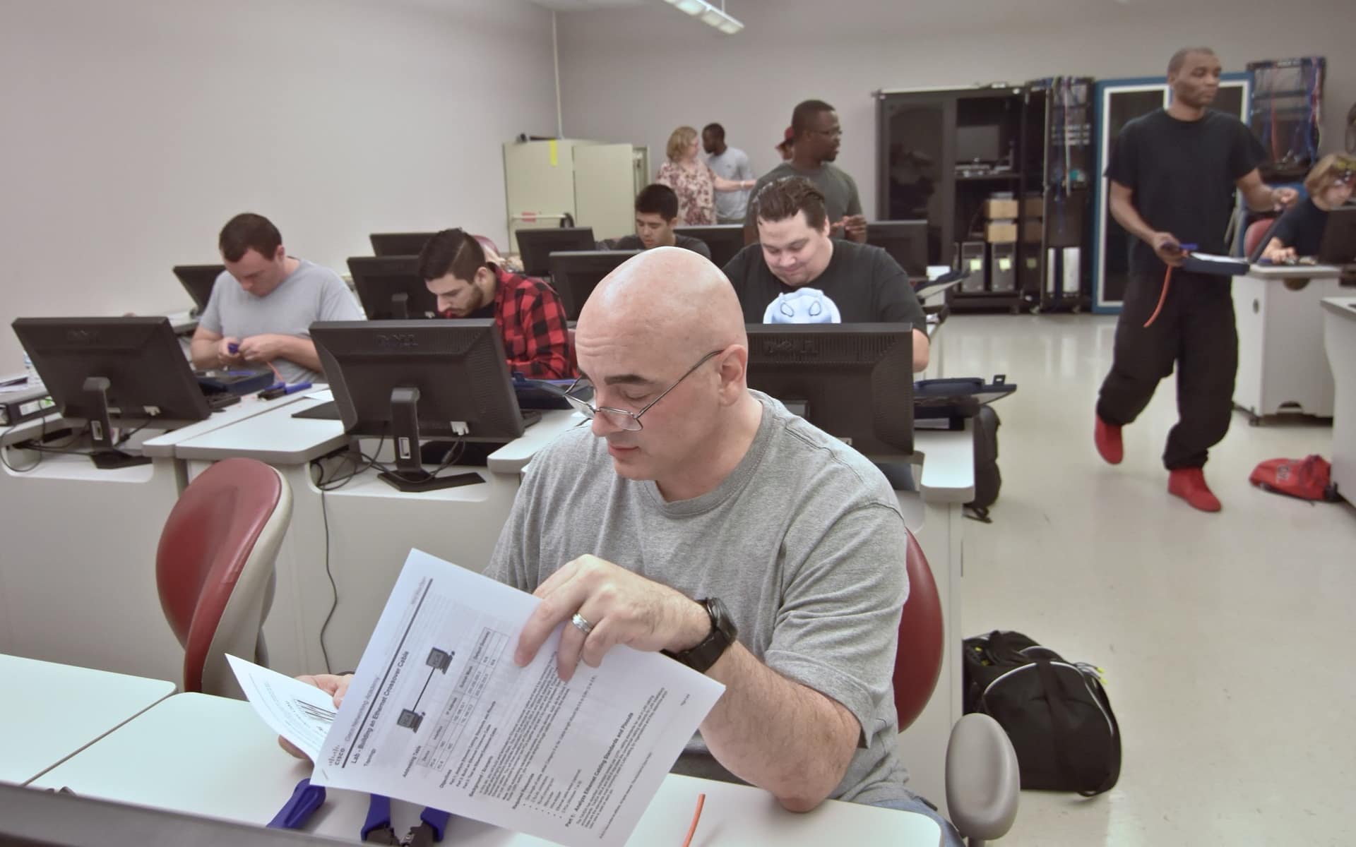 A cybersecurity training class: people at workstations, one reading through a printed exercise.